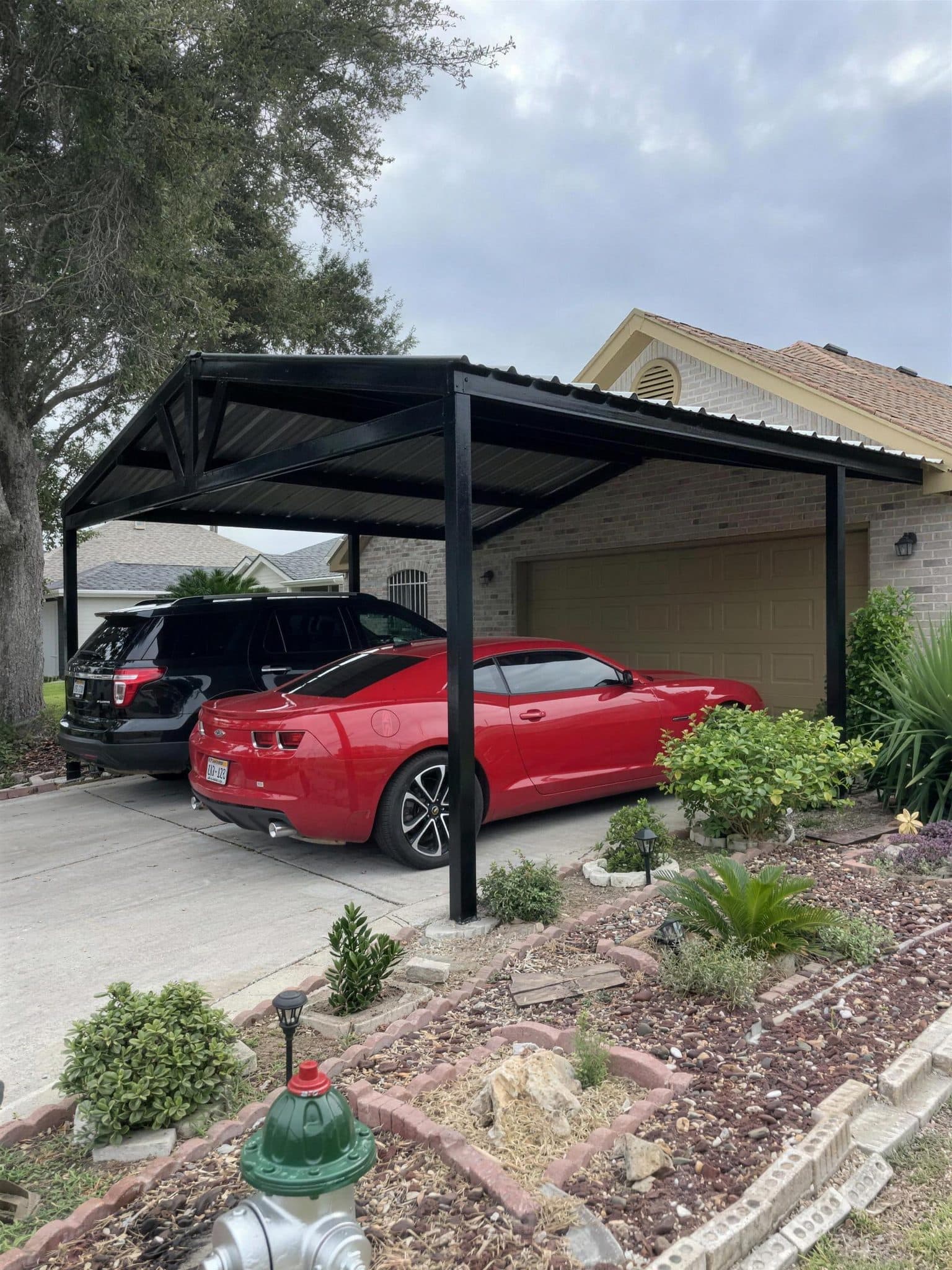 Same driveway covered by a black steel carport with two cars parked underneath