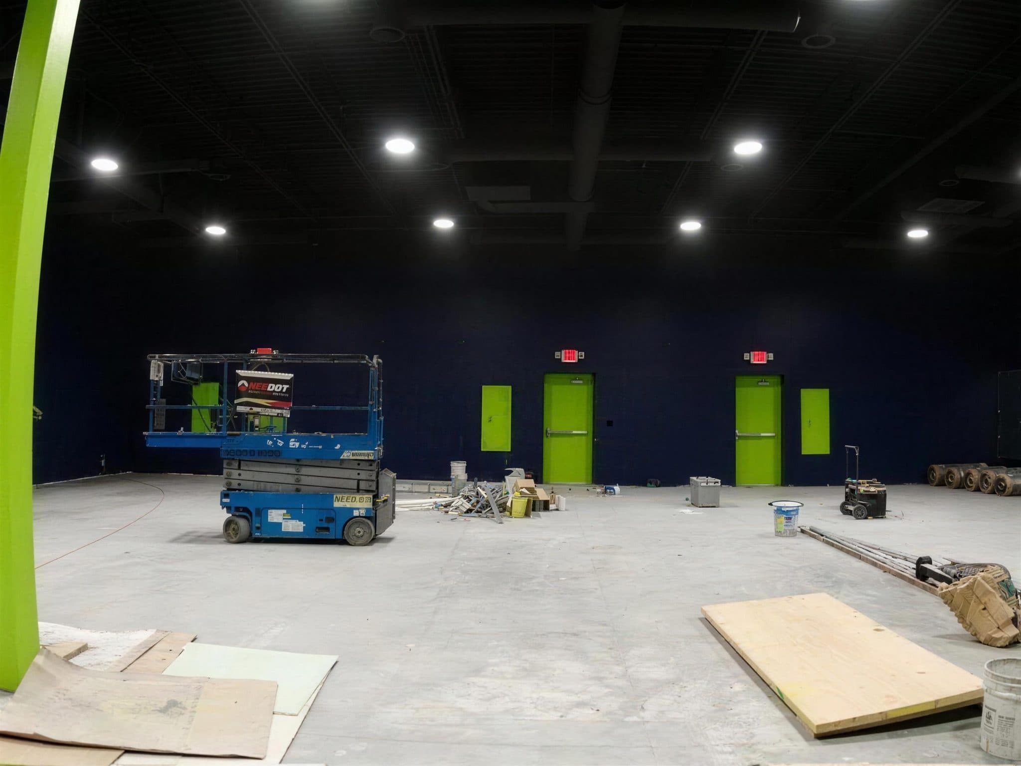 Pulze gym with navy walls, lime green doors and electrical panels, and a scissor lift on the floor.