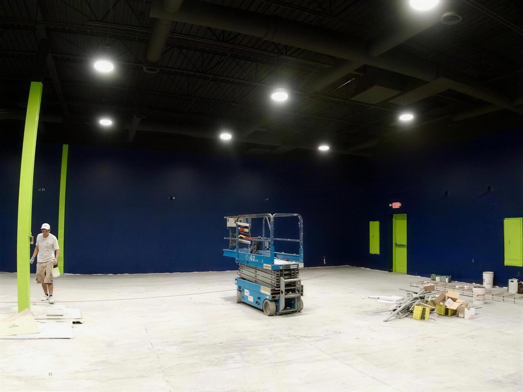 Worker walking past a lime green column with a scissor lift in the navy-walled Pulze gym.