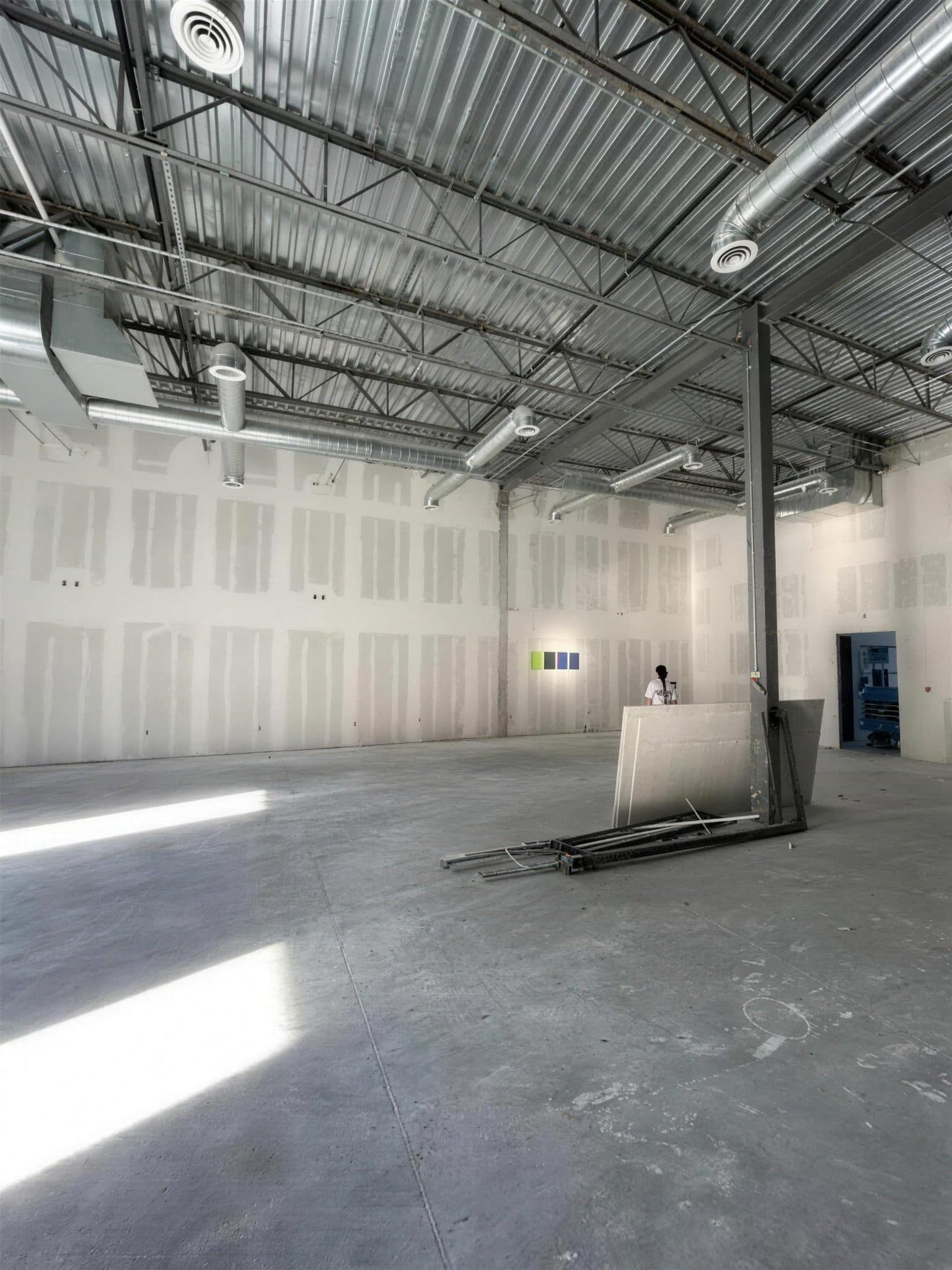Commercial interior with taped drywall walls, a steel column and sunlight across the concrete floor before painting