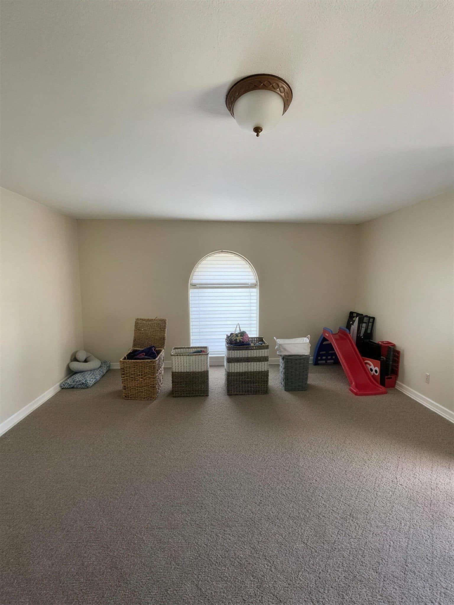 Large carpeted room with beige walls and an arched window before painting