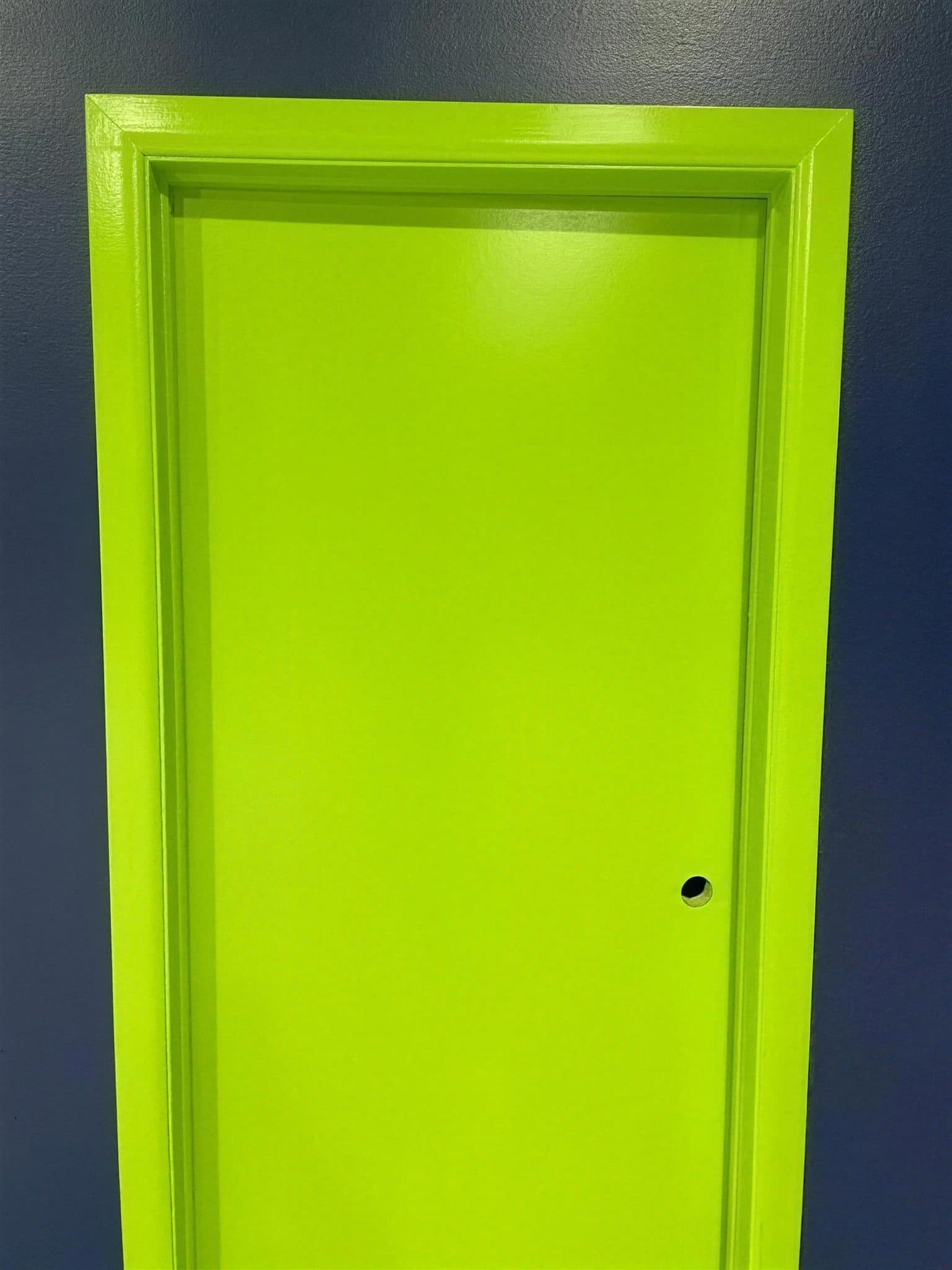 Close-up of a lime green door and frame against a navy painted wall.