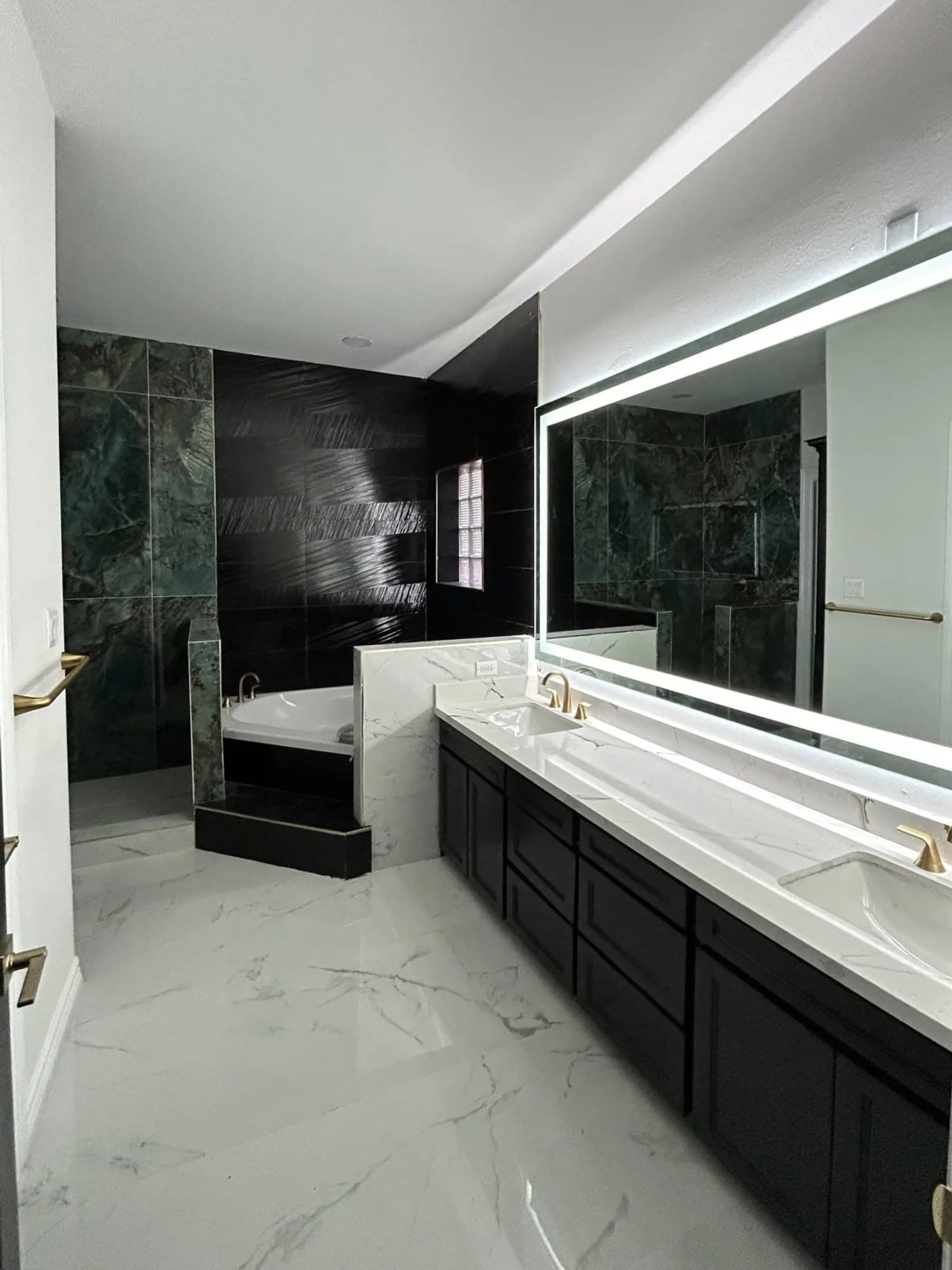Modern luxury bathroom with double marble vanity, backlit mirror, and a soaking tub with dark tile accents.