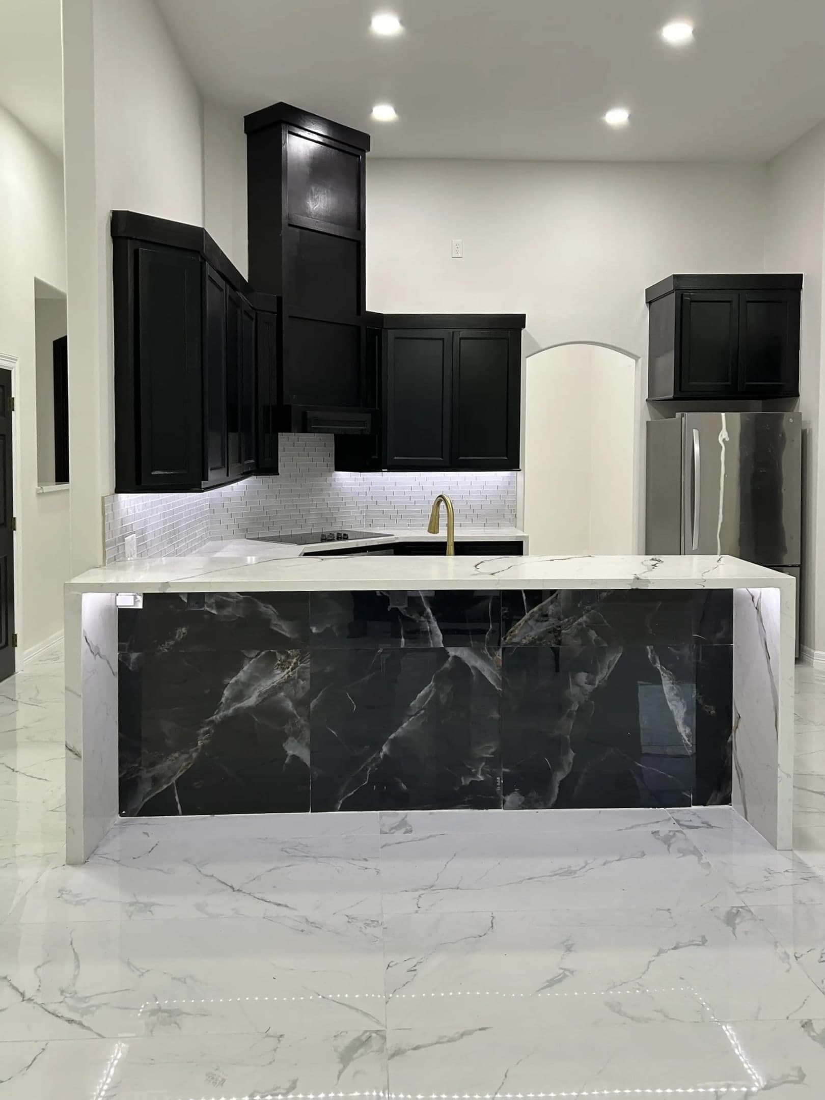 Modern luxury kitchen with black cabinets, white marble floors, and a dark marble waterfall island.