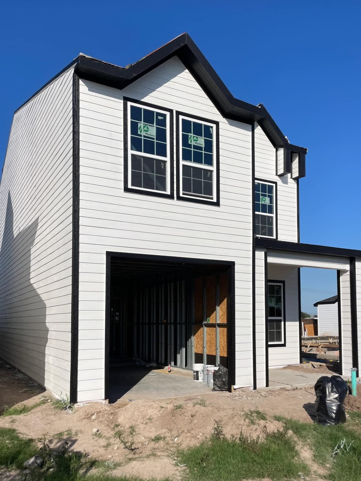 A modern two-story house under construction with white horizontal siding and black window trim.