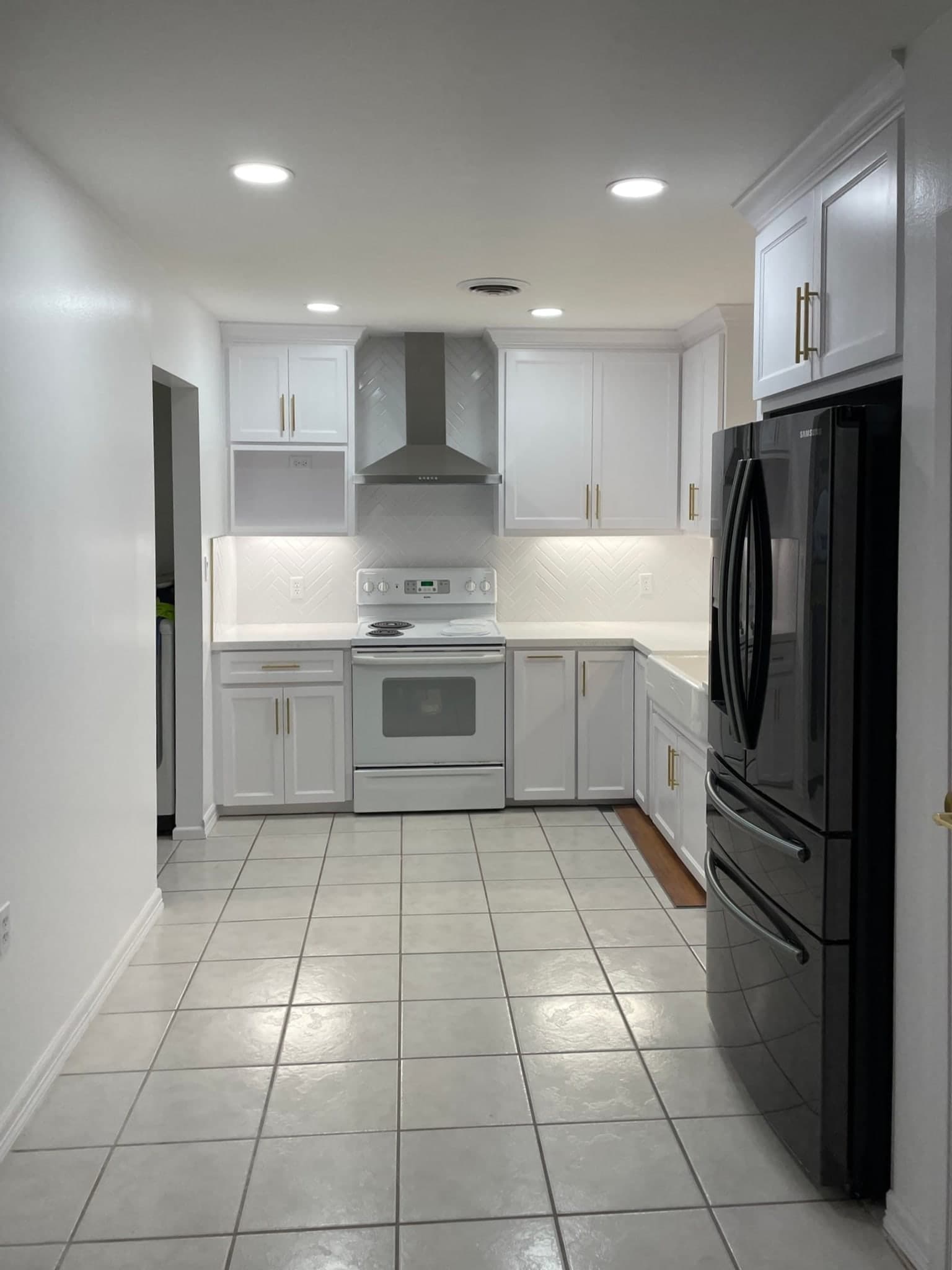 Modern white kitchen with shaker cabinets, gold hardware, and a black refrigerator.