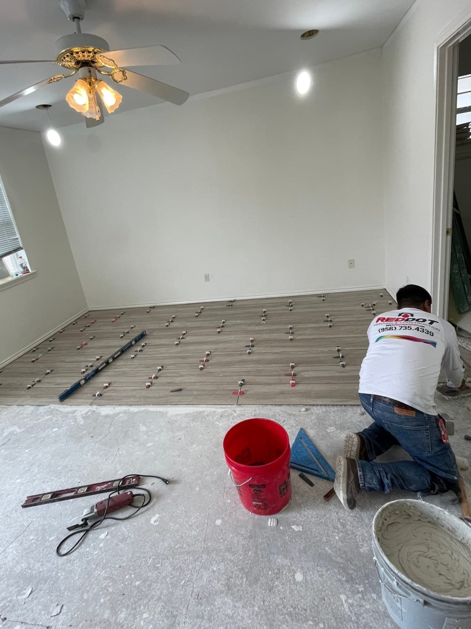 Contractor setting wood-look floor tile with a leveling system in a residential room.