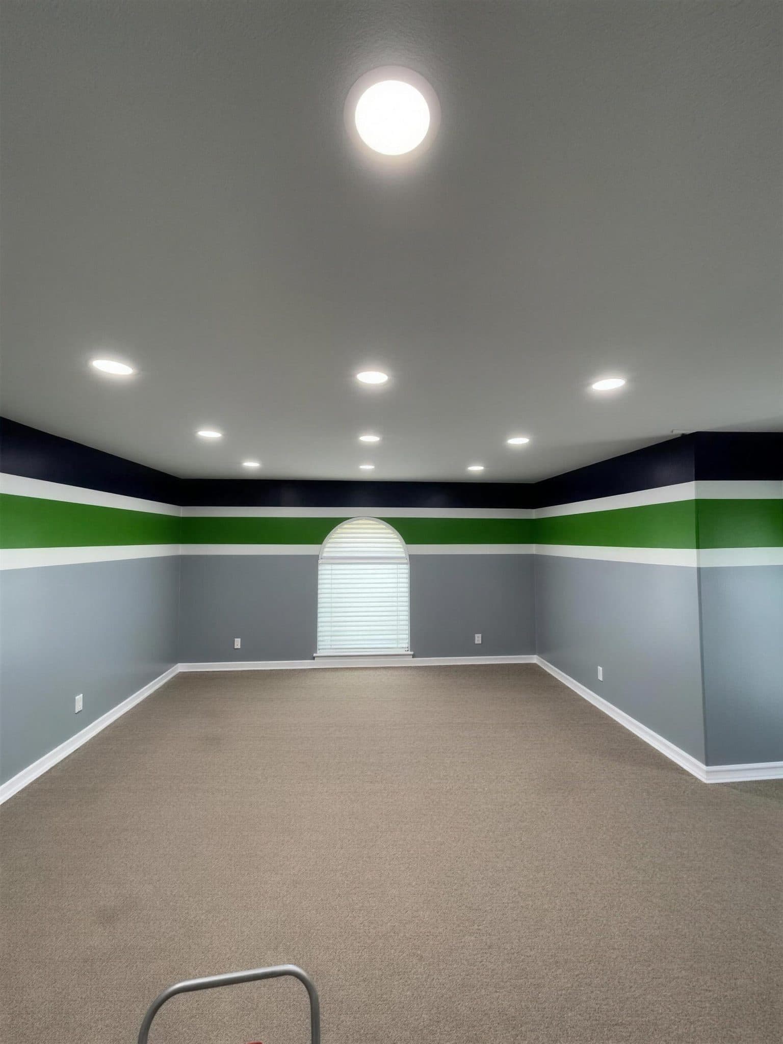 Same room after painting with gray walls under navy and green stripes and white trim, lit by recessed ceiling lights