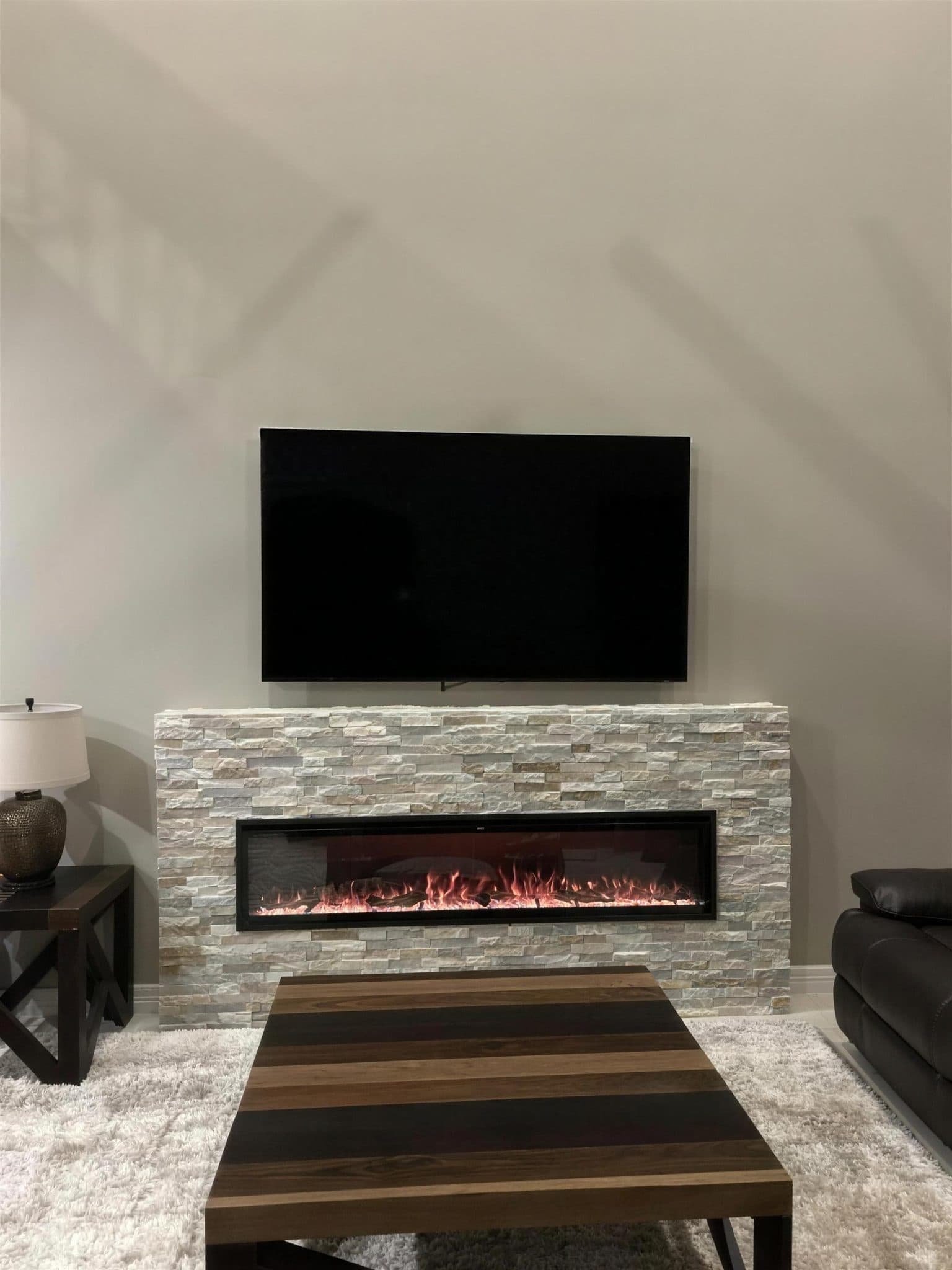 Same wall with a stacked stone surround and a built-in electric fireplace under the TV