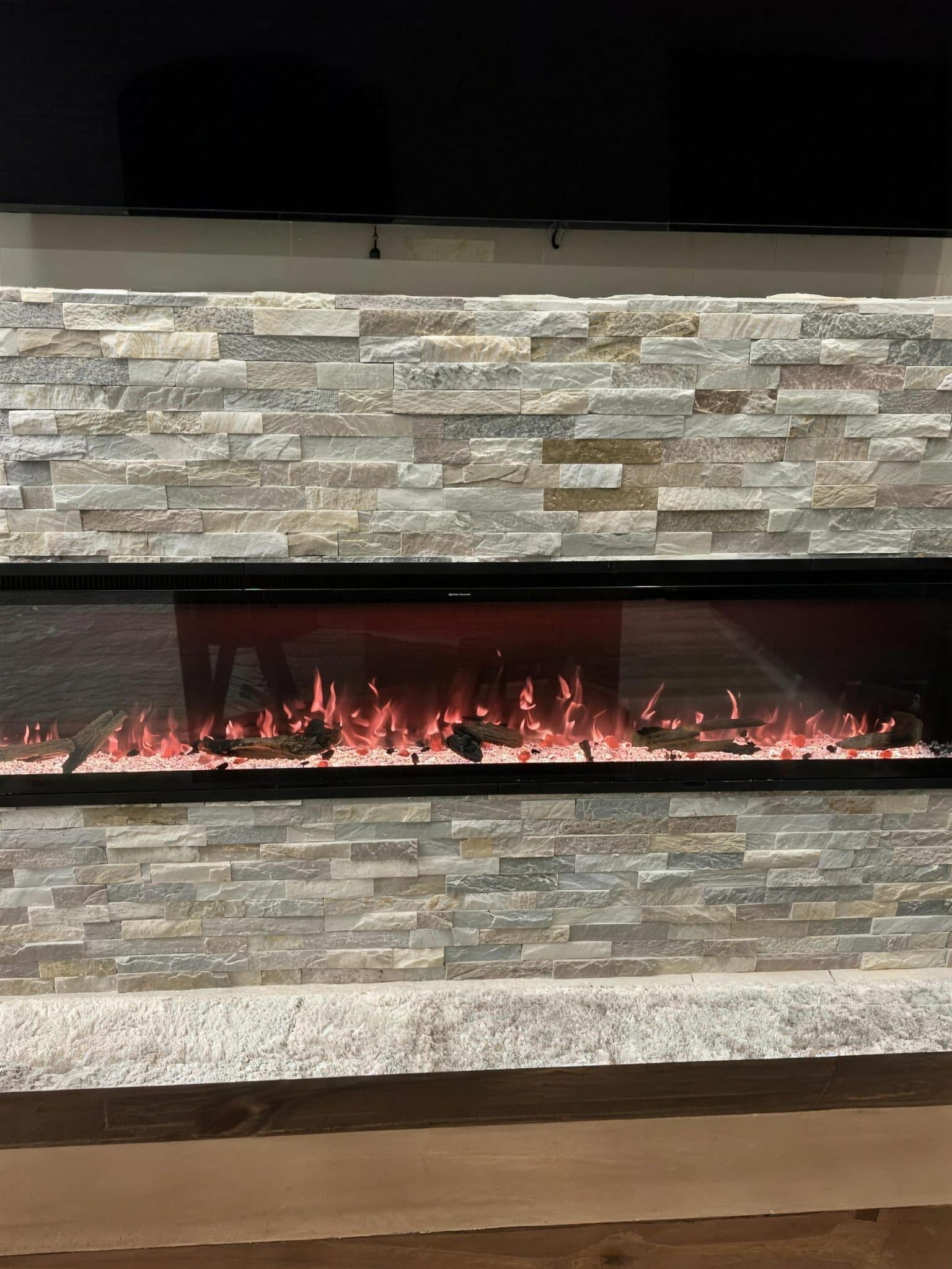 Finished stacked stone surround with the electric fireplace lit beneath the TV