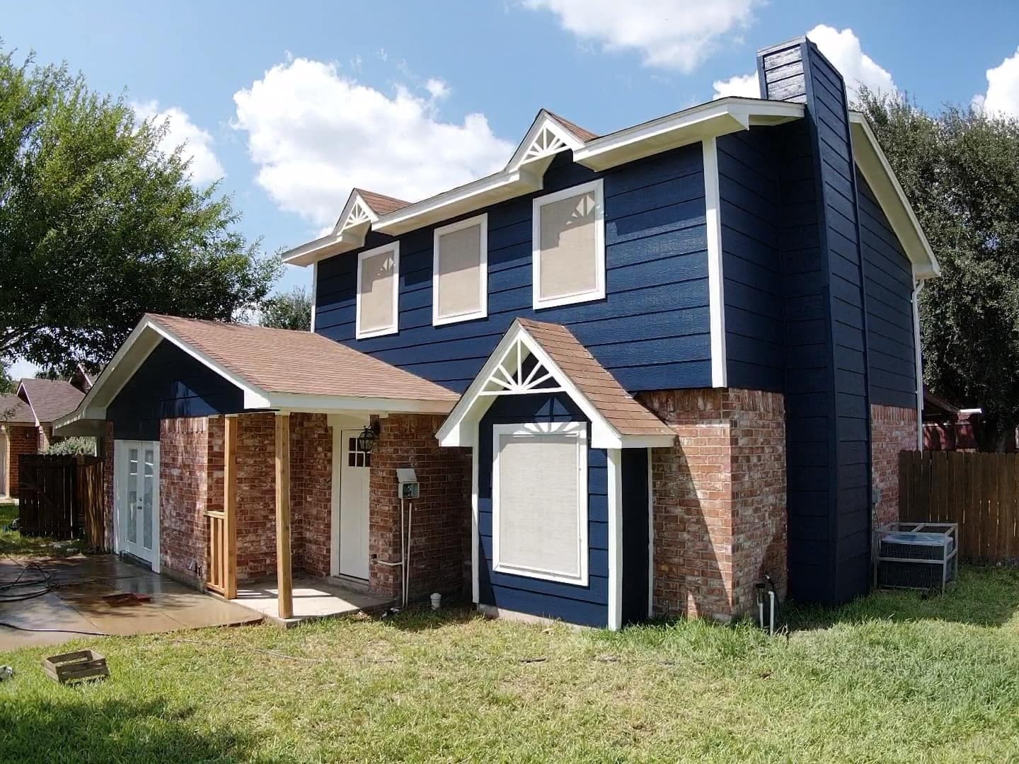 Two-story residential home featuring navy blue siding, red brick accents, and white trim architecture.